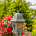 Decorative birdhouse with a garden background featuring flowers and greenery.