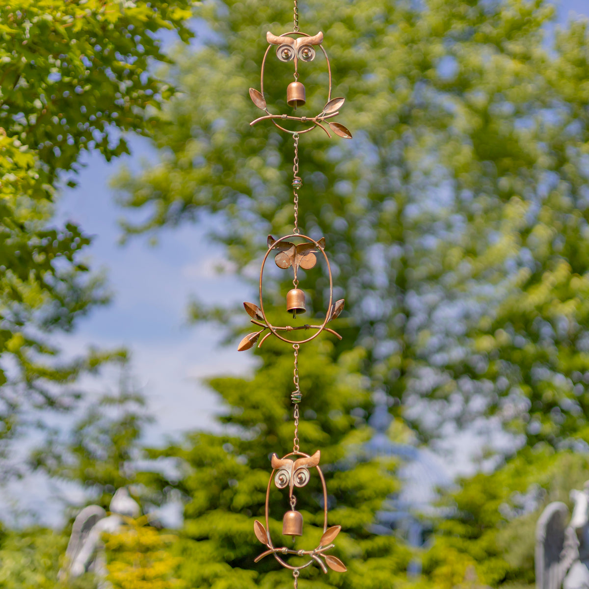 Decorative metal owl wind chime with green trees in the background