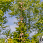Decorative metal owl wind chime with green trees in the background