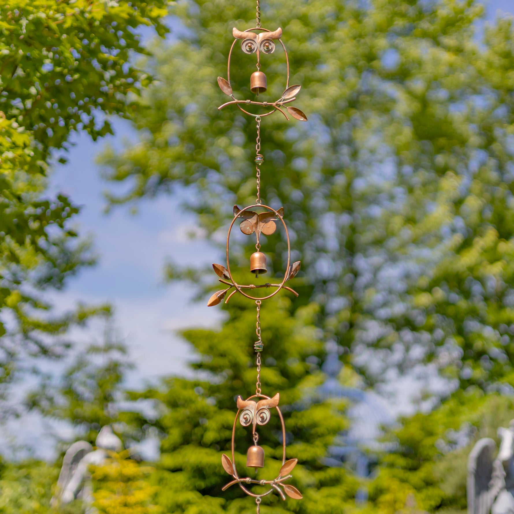 Decorative metal owl wind chime with green trees in the background