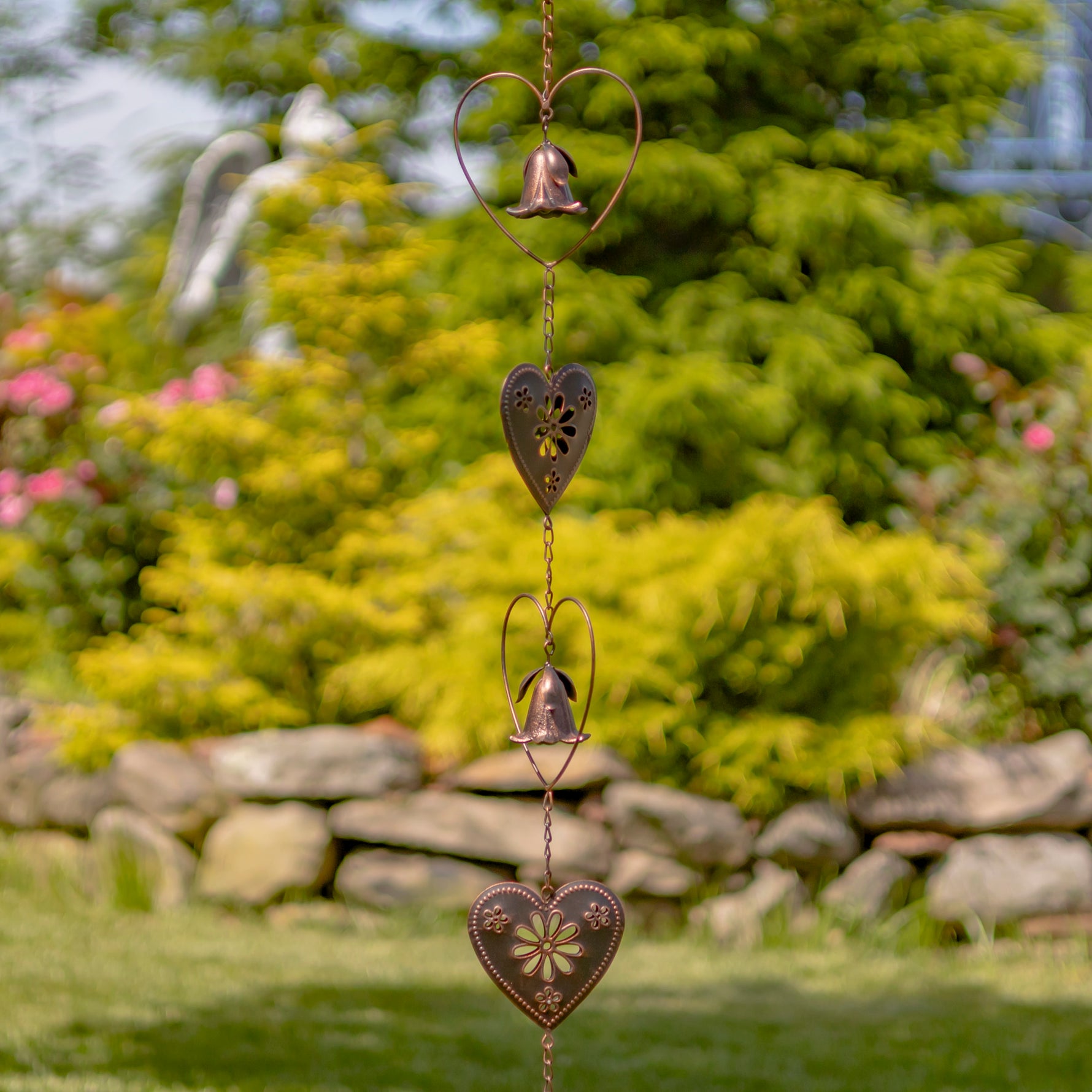 Decorative heart-shaped hanging ornament with a bell in a garden setting
