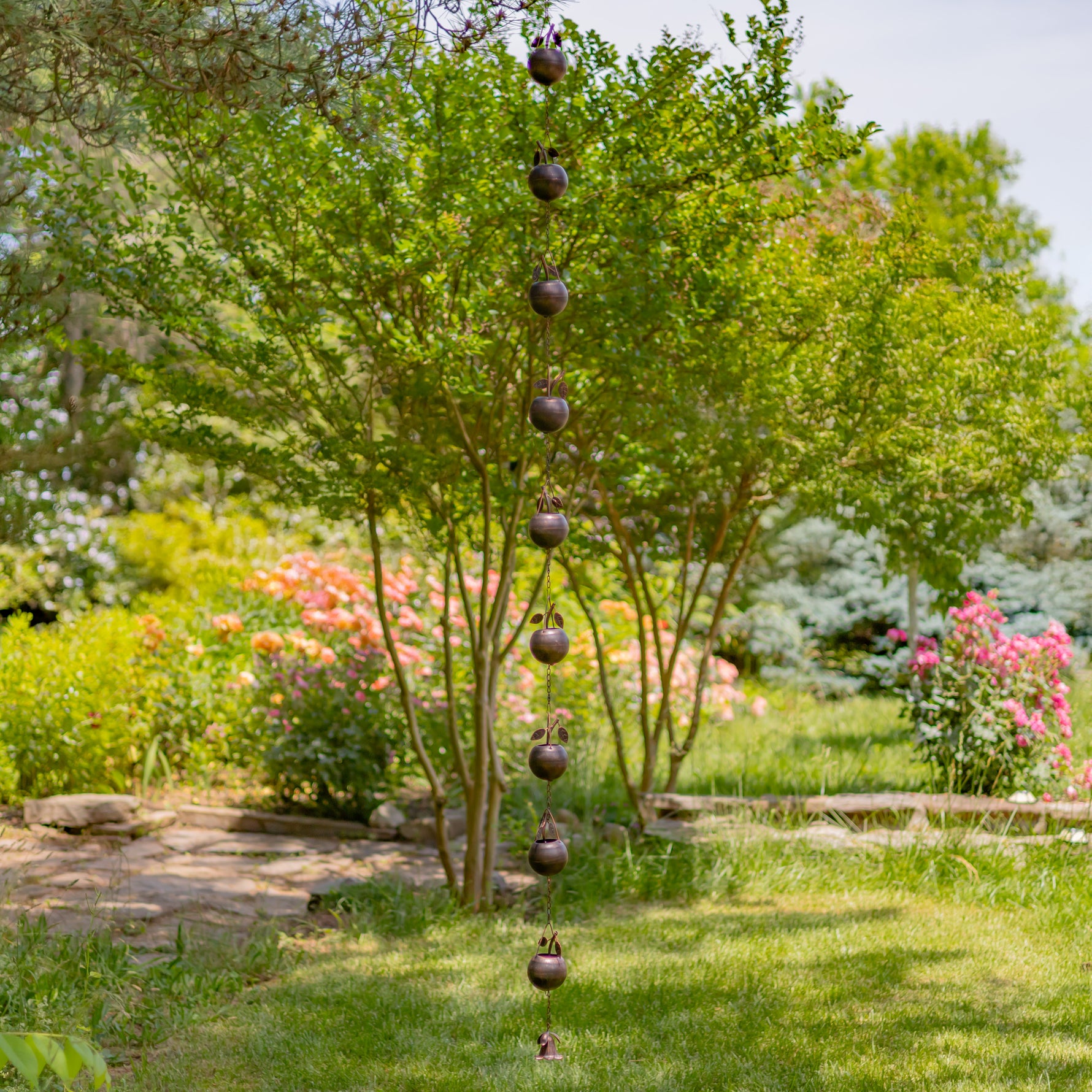 Decorative hanging mobile in a garden setting with trees and flowers.