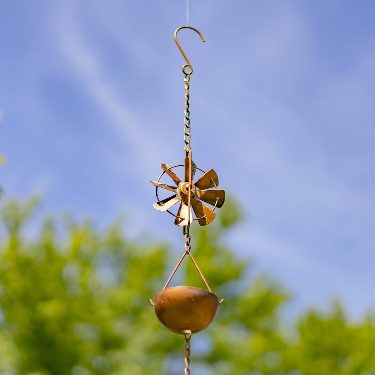 Decorative wind chime with a blue sky and green trees in the background
