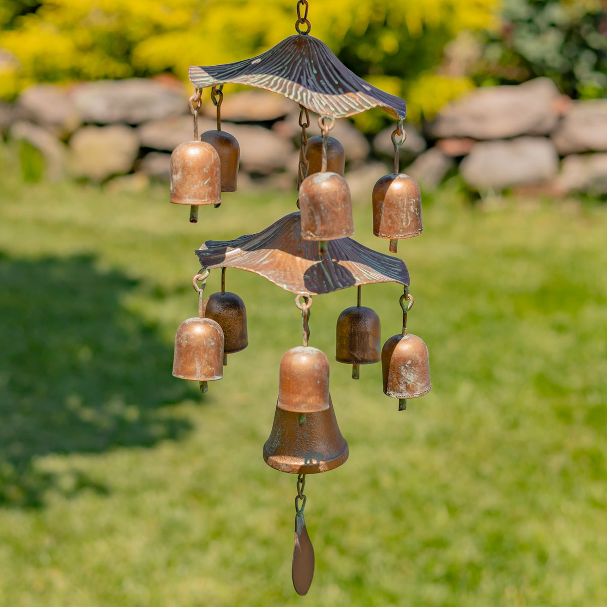 Copper bell wind chime with decorative elements on a grassy background