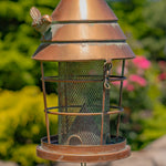 Bronze bird feeder with mesh side on a blurred garden background