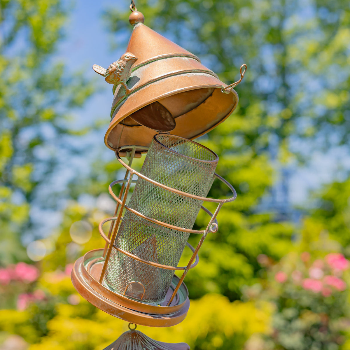 Decorative bird feeder with a cone-shaped top and mesh tube, set against a blurred natural background.