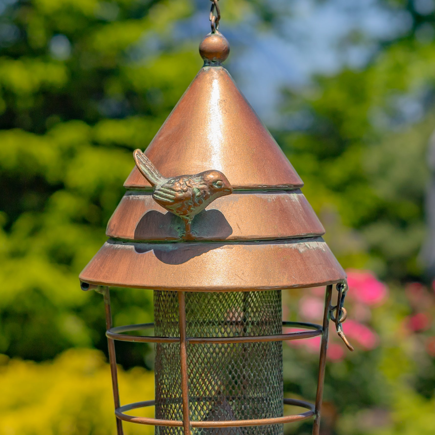 Copper bird feeder with a bird design on a blurred green garden background