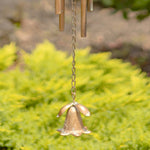 Bronze wind chime with floral design against a blurred green garden background