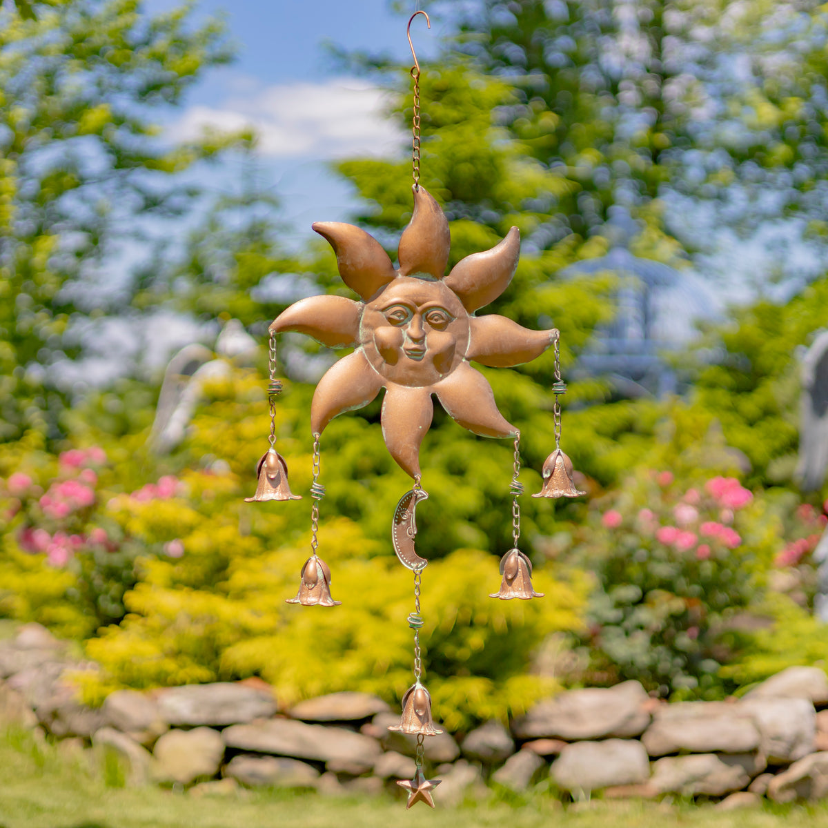 Decorative sun-shaped wind chime with hanging bells in a garden setting