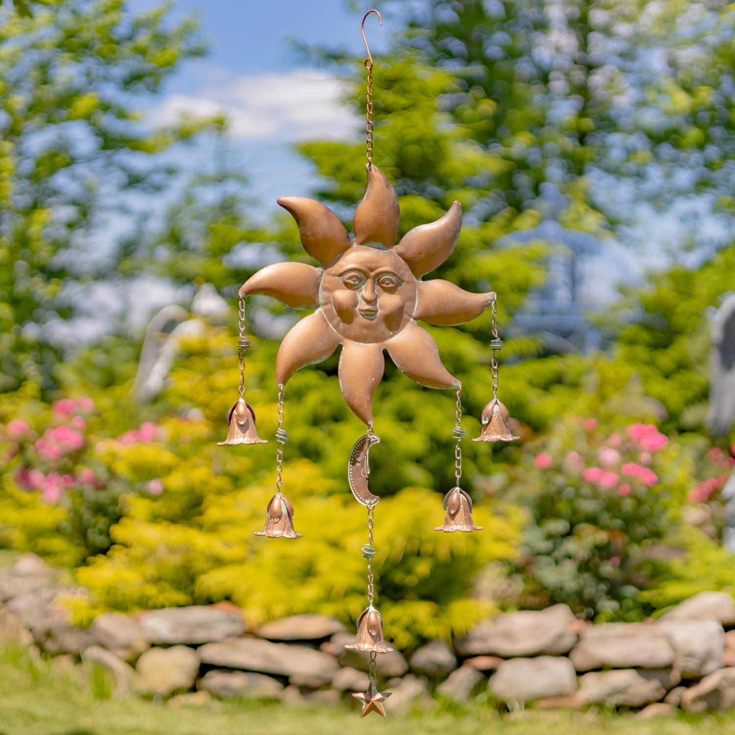 Decorative sun-shaped wind chime with hanging bells in a garden setting