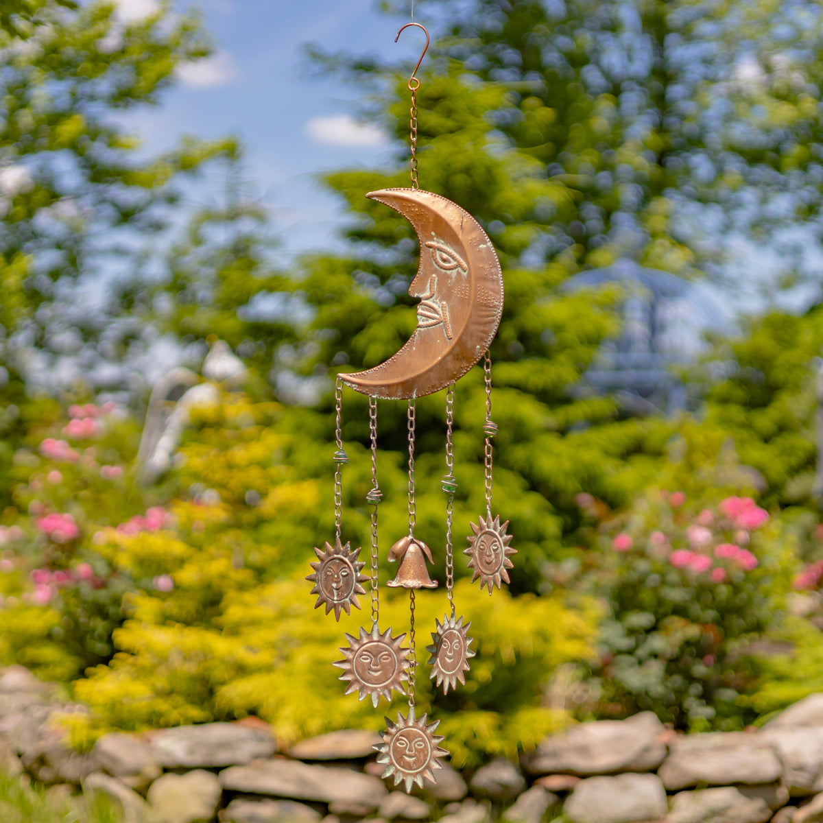 Decorative metal wind chime with celestial design hanging in a garden.