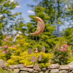 Decorative metal wind chime with celestial design hanging in a garden.