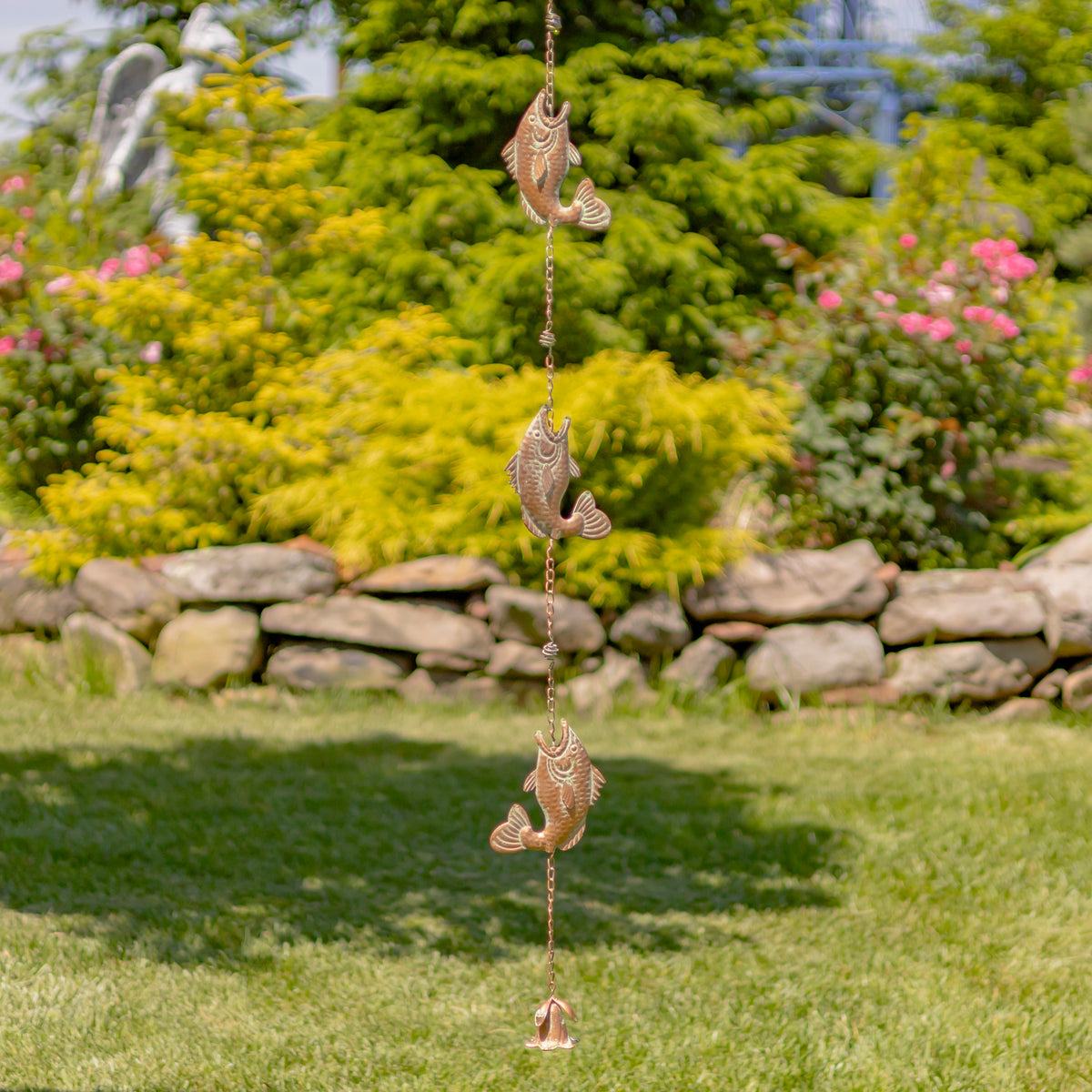 Decorative fish wind chime in a garden setting with greenery and flowers.