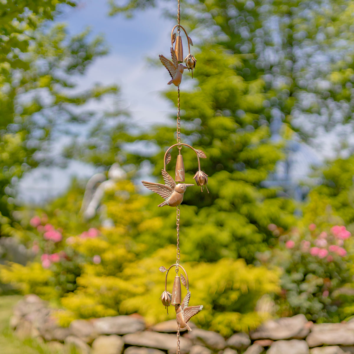 Decorative wind chime with hummingbird designs hanging against a garden backdrop.
