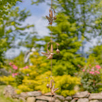 Decorative wind chime with hummingbird designs hanging against a garden backdrop.
