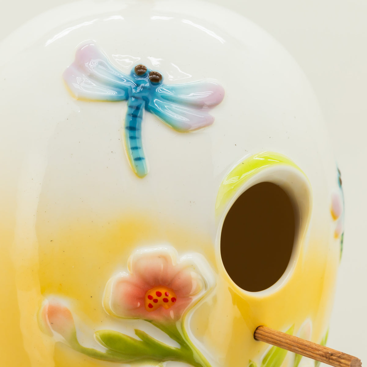 Ceramic birdhouse with a dragonfly and flower design on a white background