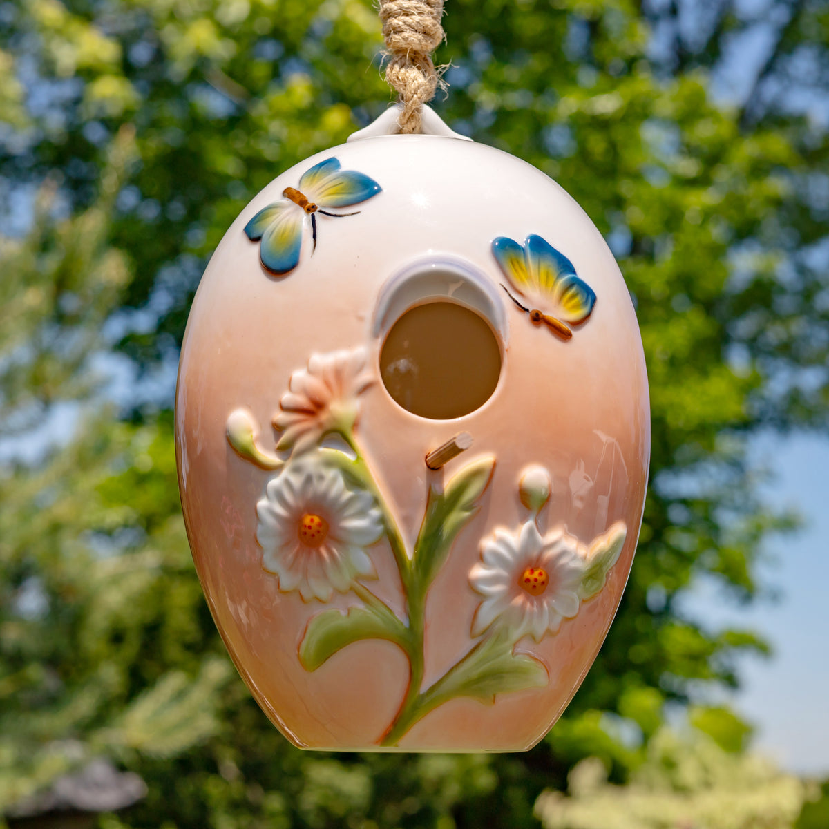 Decorative birdhouse with floral designs and butterfly accents hanging against a natural background.