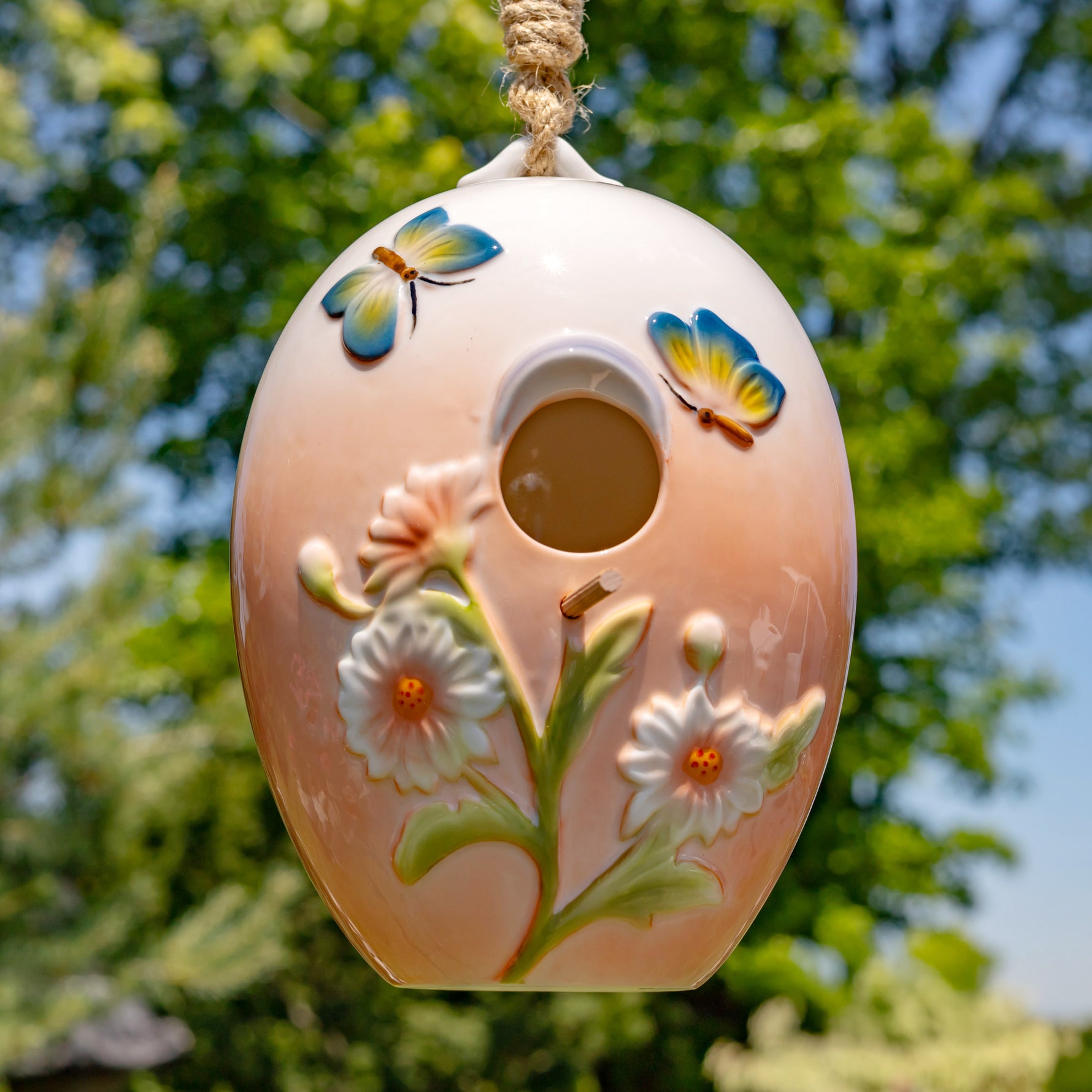 Decorative birdhouse with floral designs and butterfly accents hanging against a natural background.