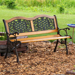 Wooden and iron bench sitting in mulch in front of a grassy meadow.