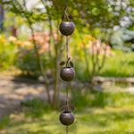 Decorative metal wind chime with three hanging bowls in a garden setting