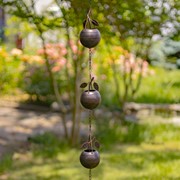 Decorative metal wind chime with three hanging bowls in a garden setting