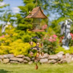 Birdfeeder and windchime hanging on green tree with lovely garden background