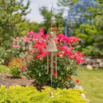 Decorative wind chime in a garden with pink flowers and greenery.