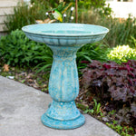 Turquoise bird bath in a garden setting with a bird perched on it.