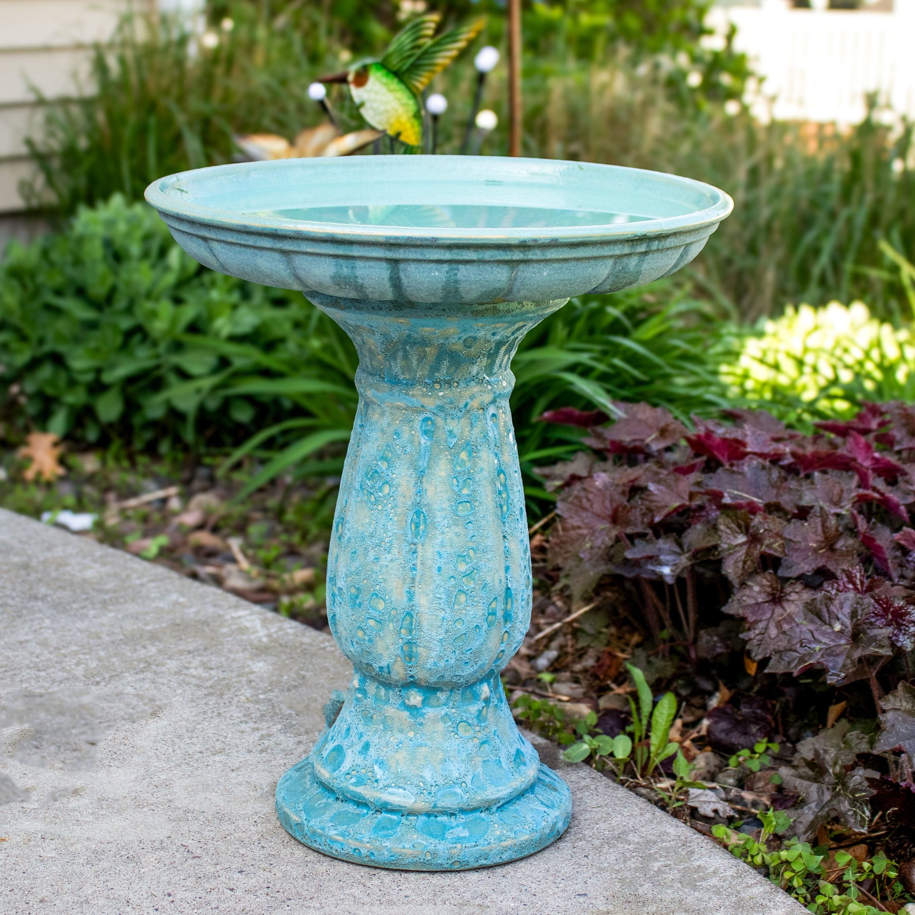 Turquoise bird bath in a garden setting with a bird perched on it.