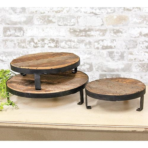 Set of three round wooden stands with metal legs against a stone wall background