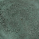 A close-up of a textured material swatch in a muted teal-green color with a fine grain and subtle darker veining.