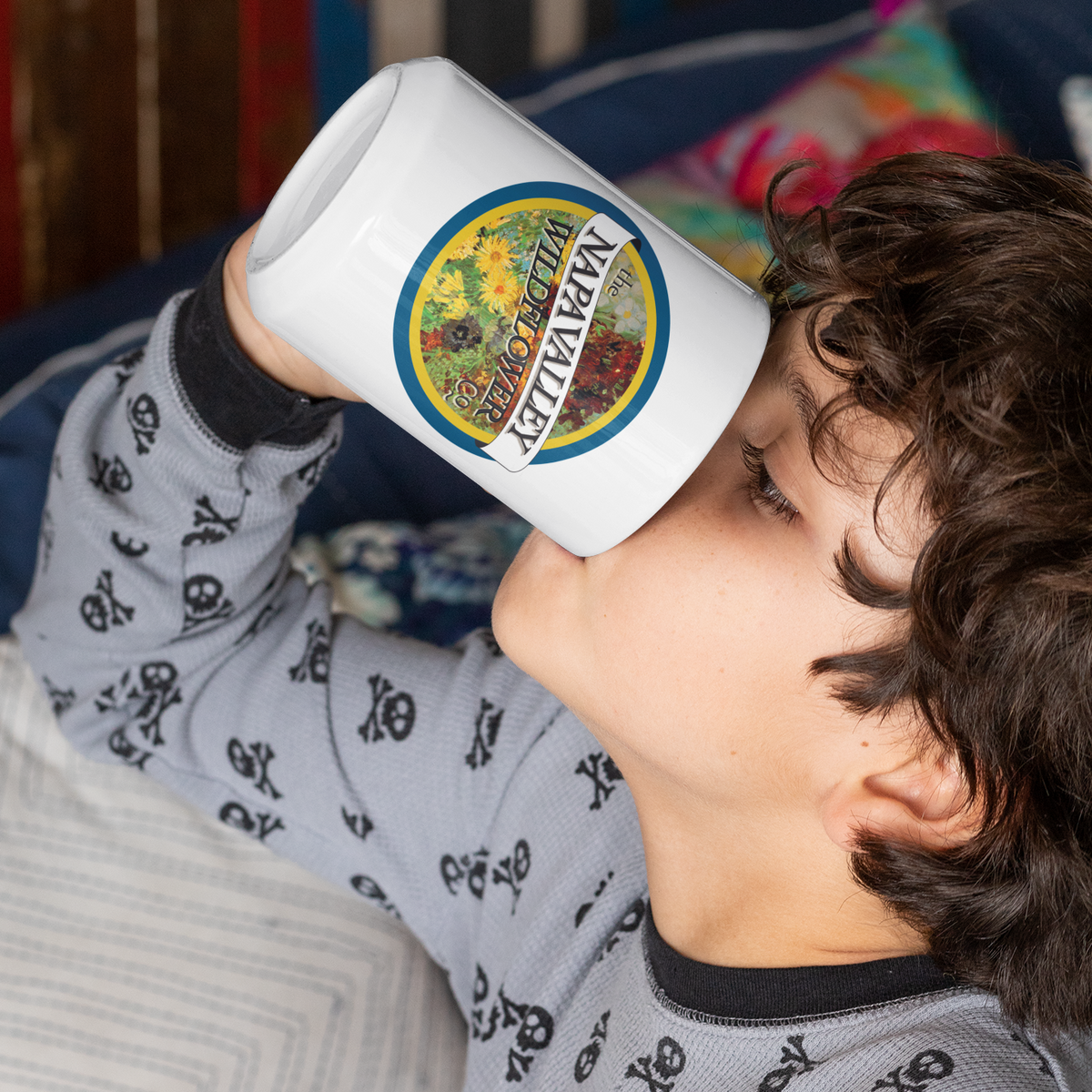 Child drinking from a white mug with a colorful label, wearing a gray pajama shirt with black patterns.