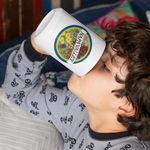 Child drinking from a white mug with a colorful label, wearing a gray pajama shirt with black patterns.