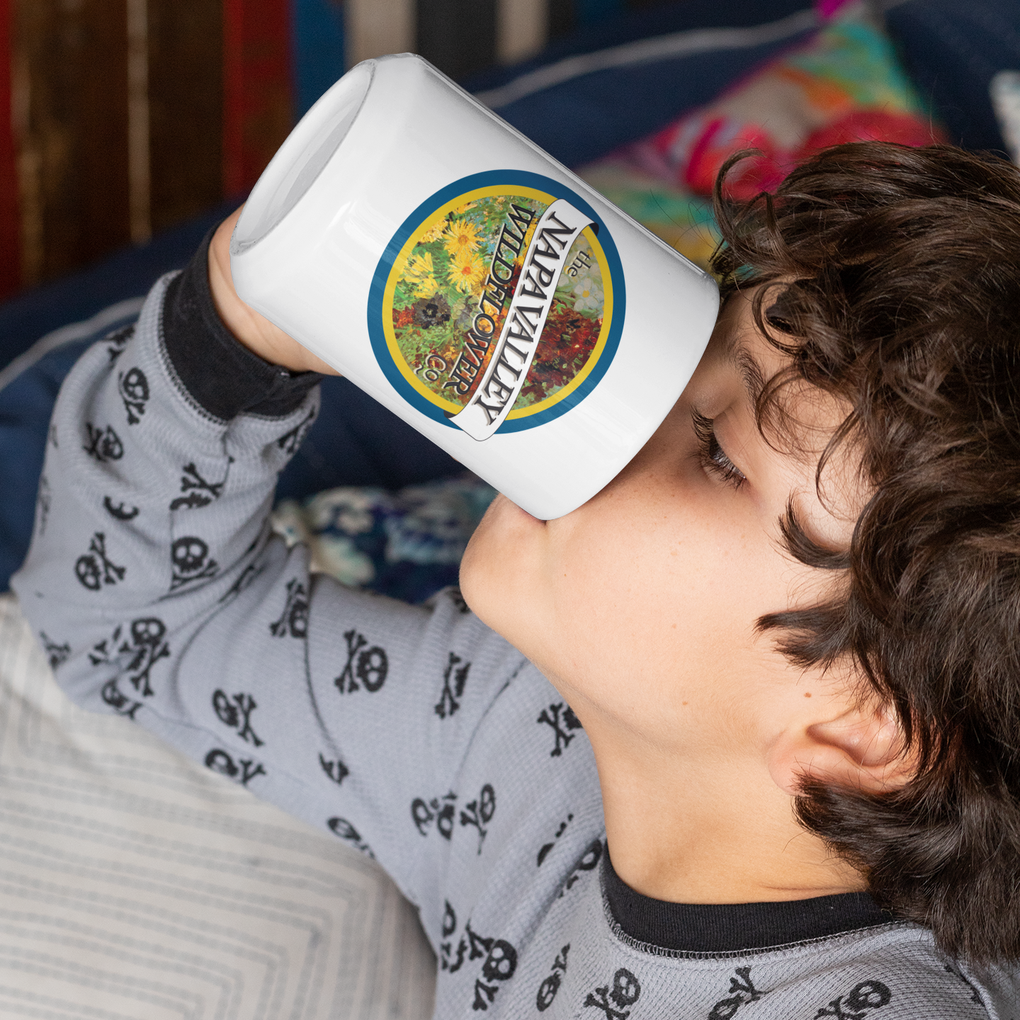 Child drinking from a white mug with a colorful label, wearing a gray pajama shirt with black patterns.
