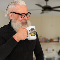 Man with gray hair and beard holding a mug in a kitchen