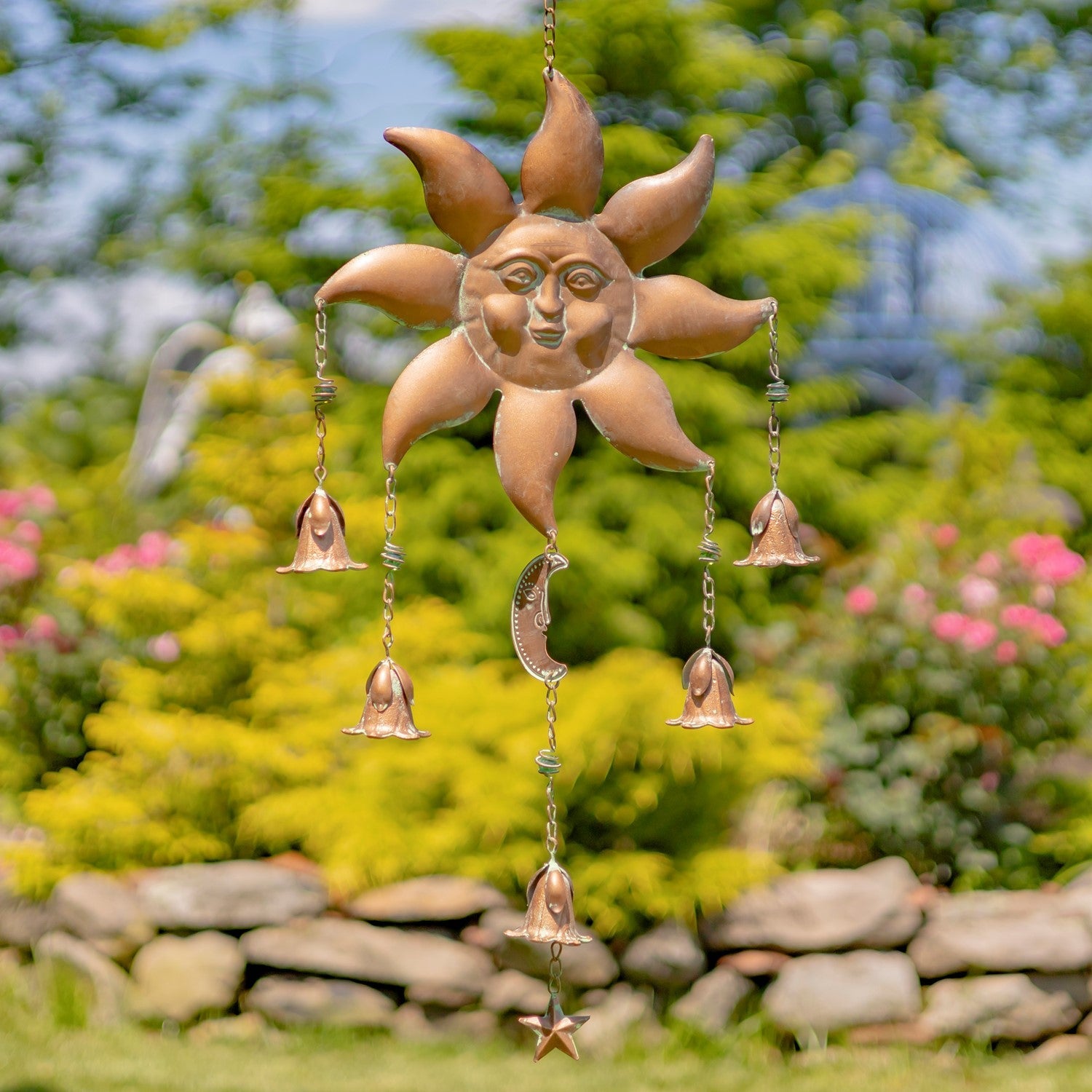 Decorative sun-shaped wind chime with hanging bells against a garden background
