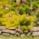 Copper wind chime with bells and moon design hanging against a natural background.