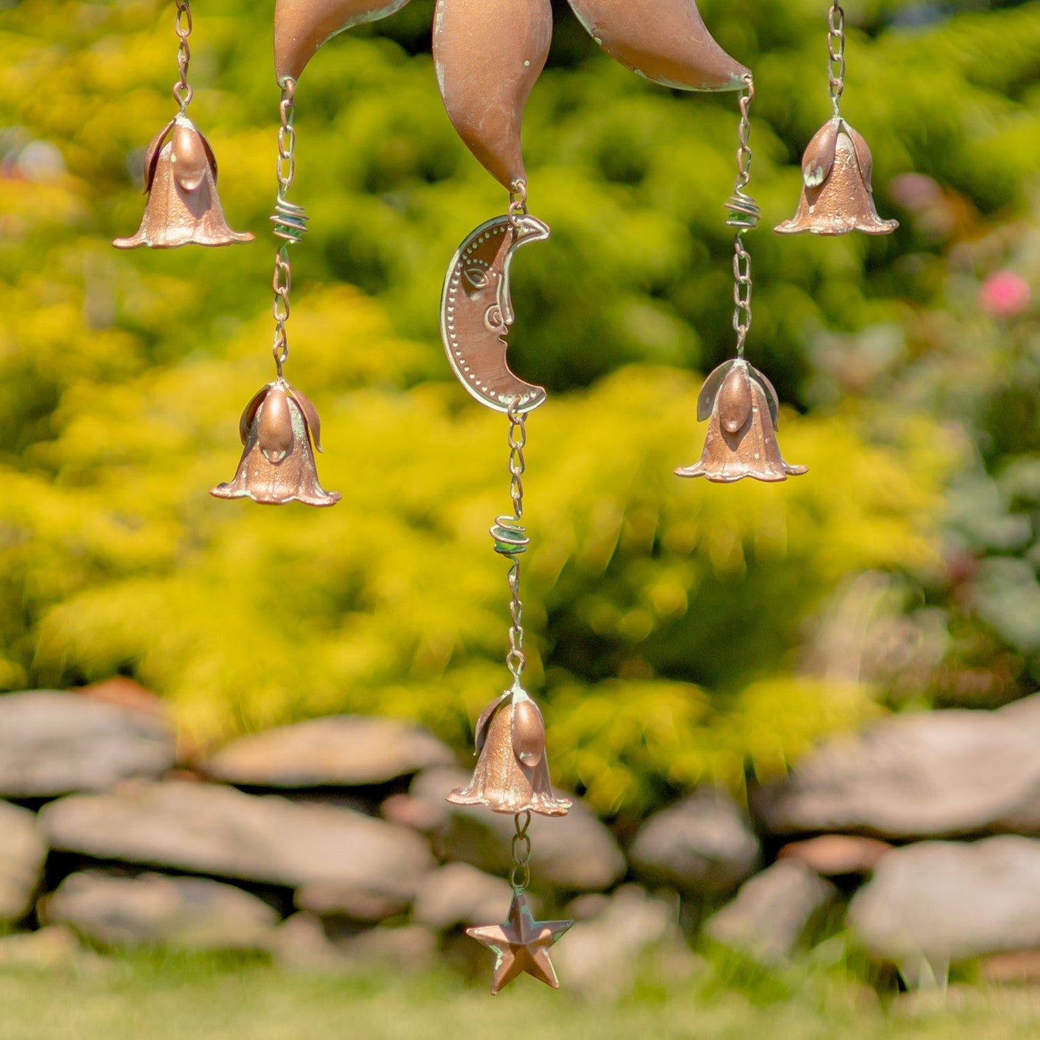 Copper wind chime with bells and moon design hanging against a natural background.