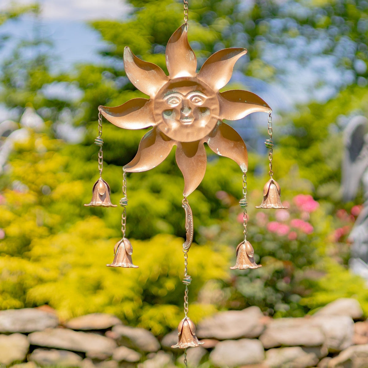 Copper sun-shaped wind chime with hanging bells against a garden background