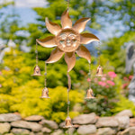 Copper sun-shaped wind chime with hanging bells against a garden background