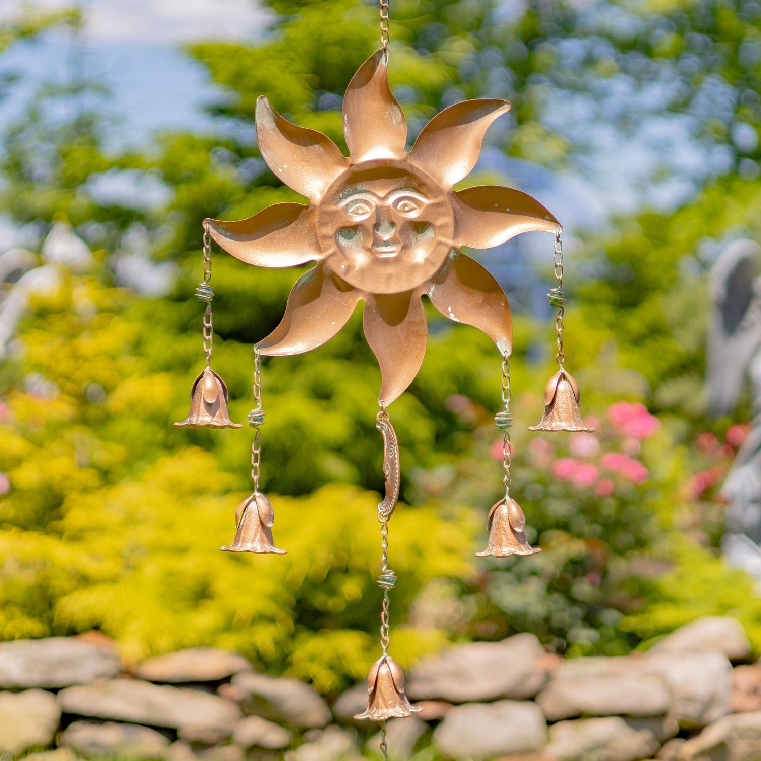 Copper sun-shaped wind chime with hanging bells against a garden background