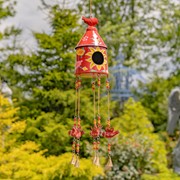 Decorative birdhouse with a red top hanging in a garden.