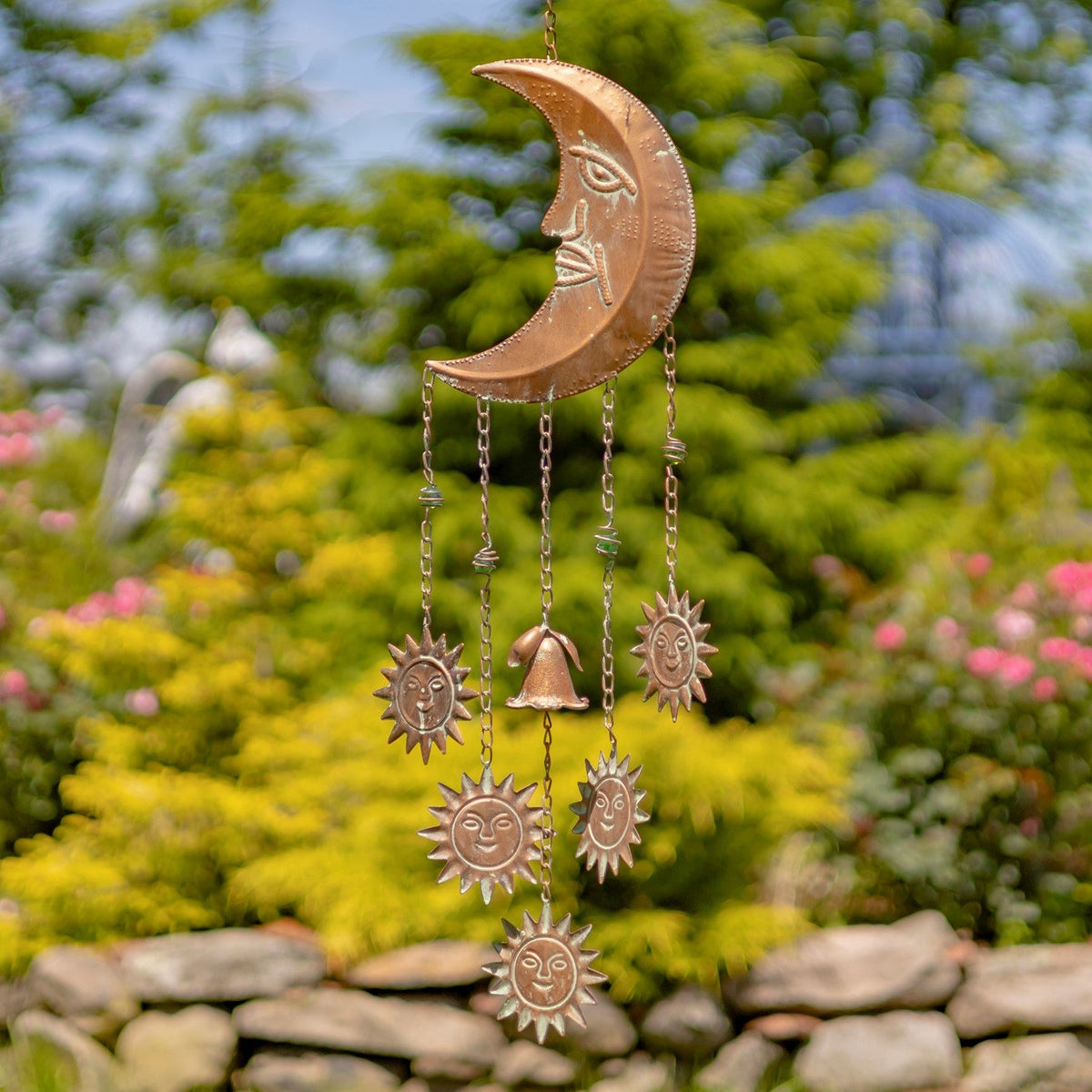Decorative copper wind chime with celestial designs in a garden setting