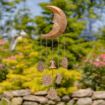 Decorative copper wind chime with celestial designs in a garden setting