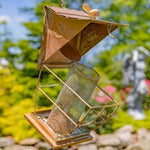 Decorative metal bird feeder with glass panels in an outdoor setting