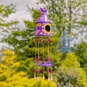 Decorative purple birdhouse with hanging elements against a blurred natural background