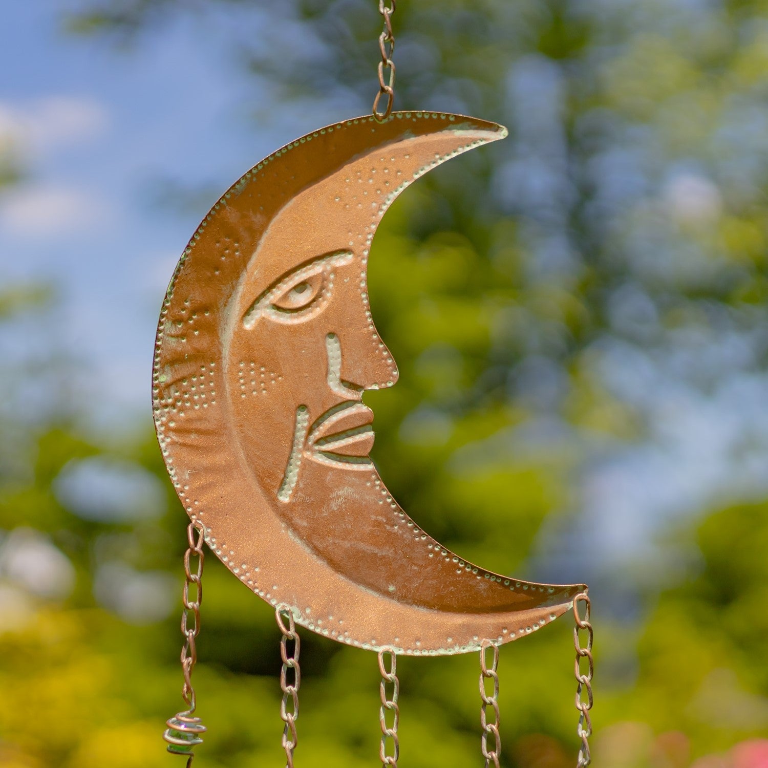 Decorative metal crescent moon with face design hanging against a blurred natural background