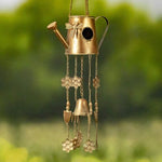 Decorative wind chime shaped like a watering can with hanging charms against a green background