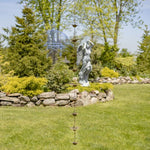 Decorative metal rain chain in a garden setting with trees and rocks.
