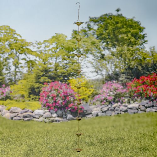 Decorative hanging rain chain in a garden setting with flowers and trees.